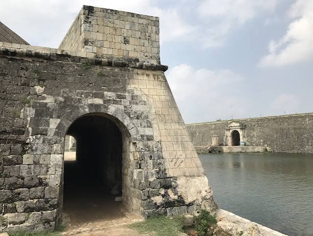 Historic stone fortress with arched passage beside calm coastal water.