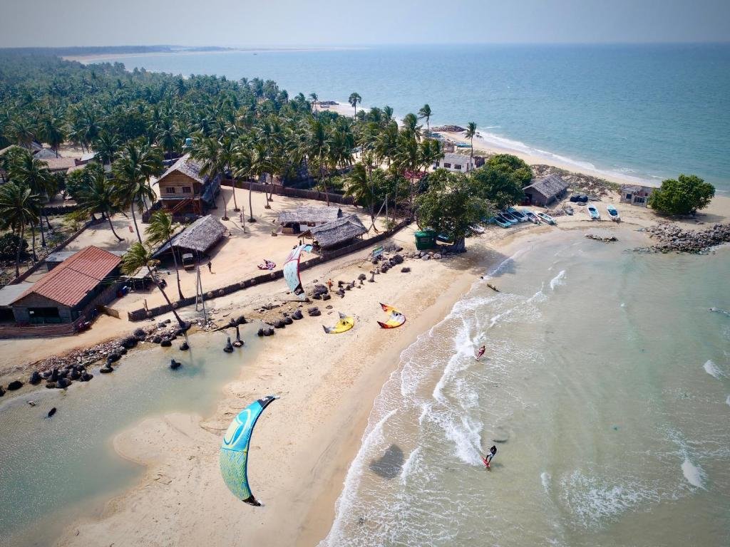Aerial view of tropical beach village with palm trees, turquoise water, and kiteboarding.