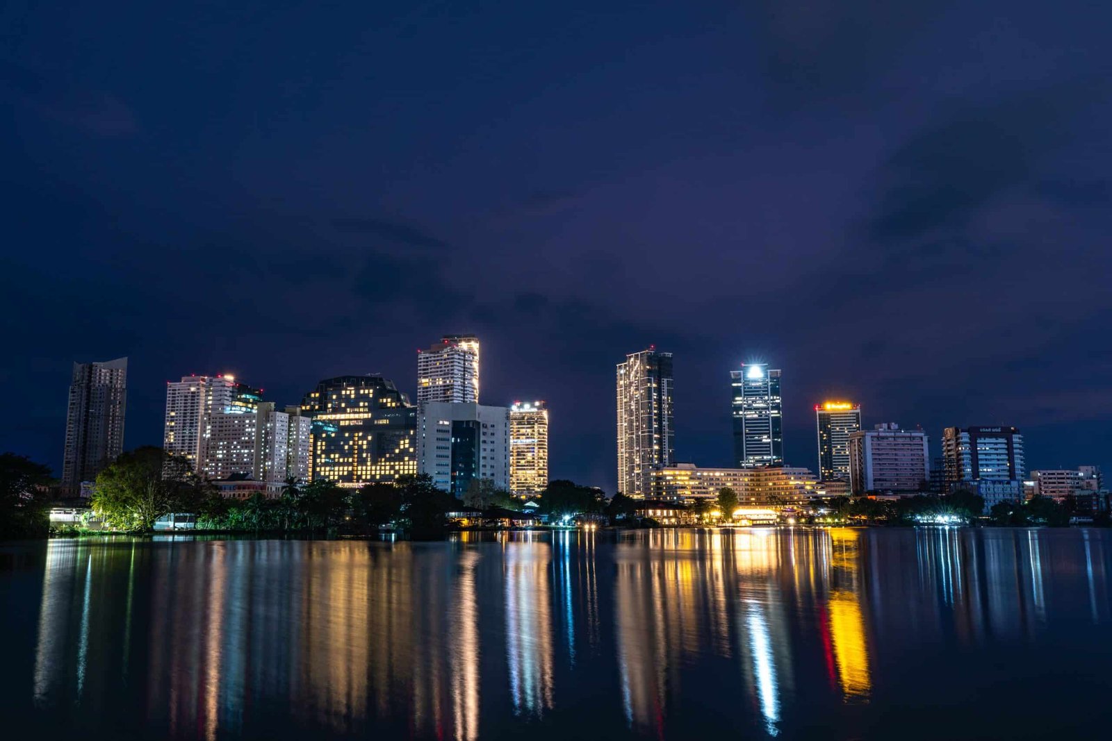Night city skyline reflecting blue, green, and golden lights across calm water.