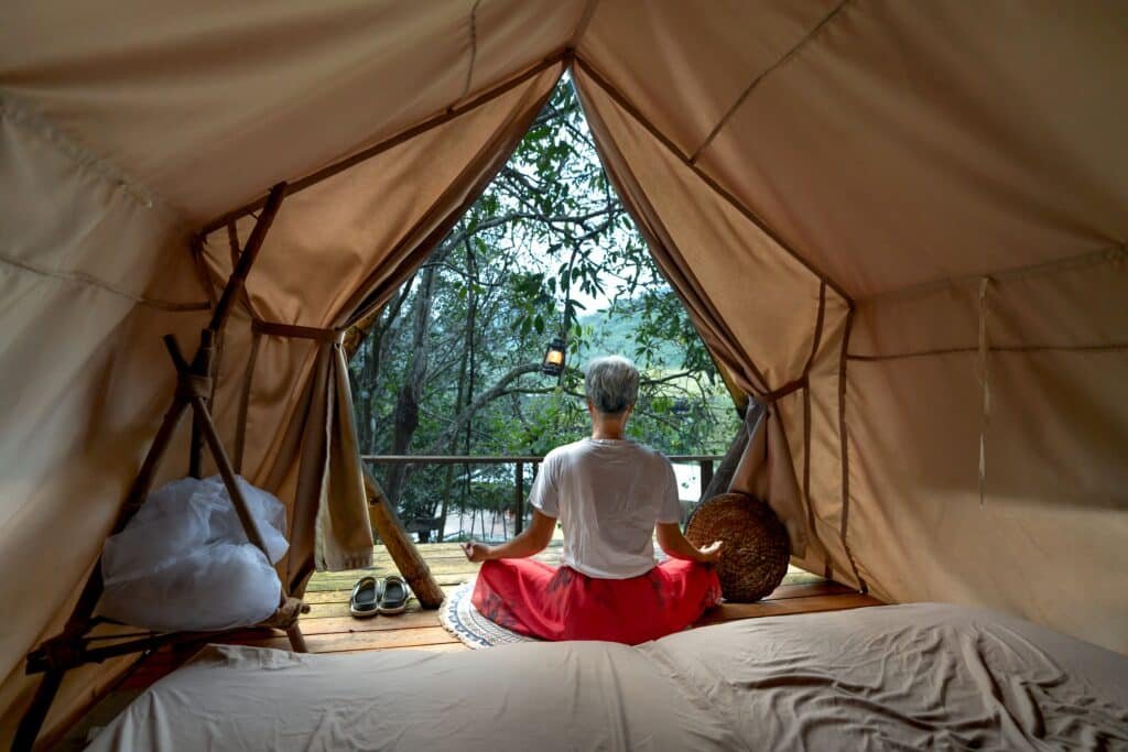 Person relaxing inside a cozy canvas tent overlooking a peaceful woodland lake.