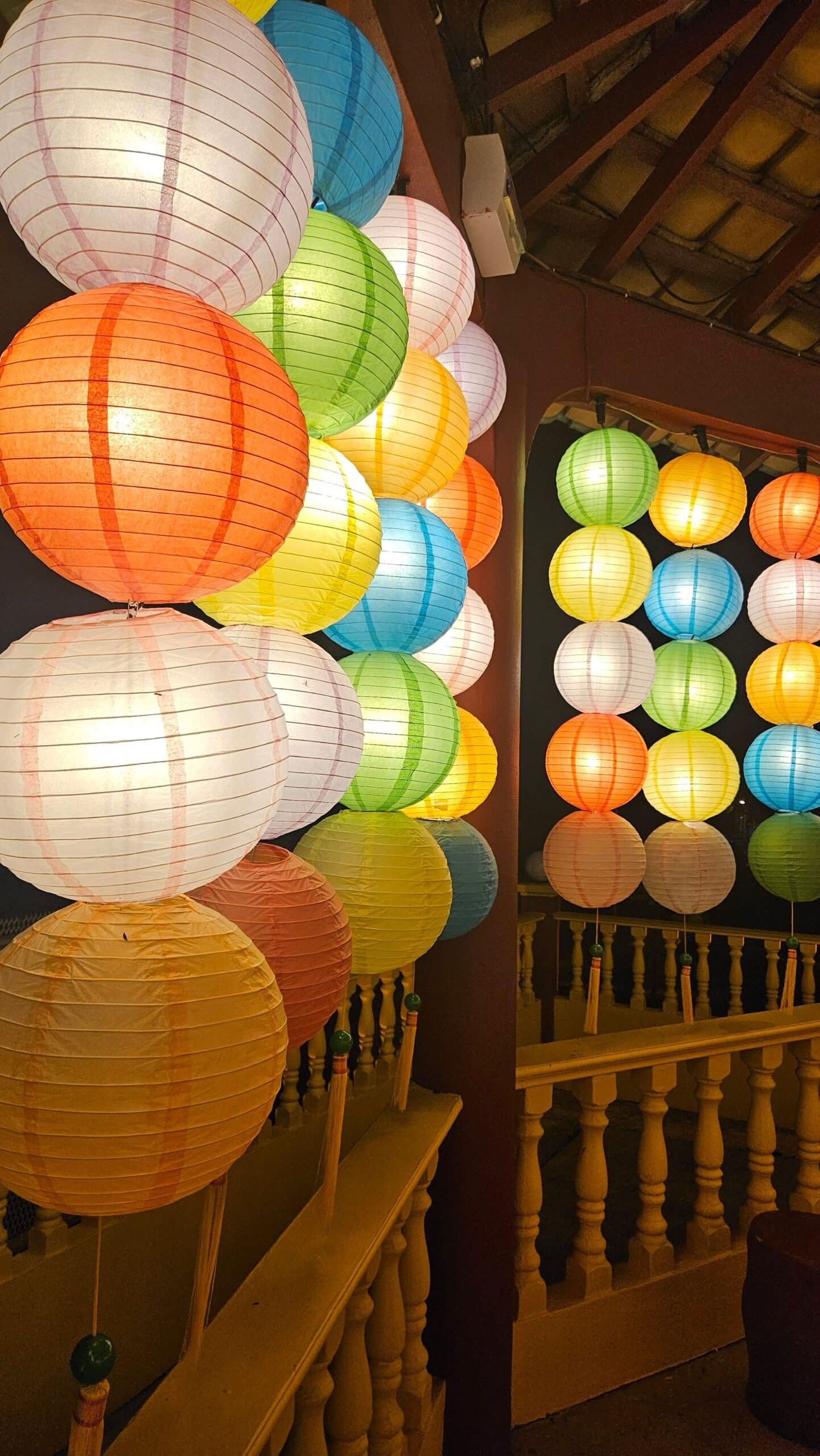 Colorful paper lanterns illuminate a rustic wooden staircase and balcony.
