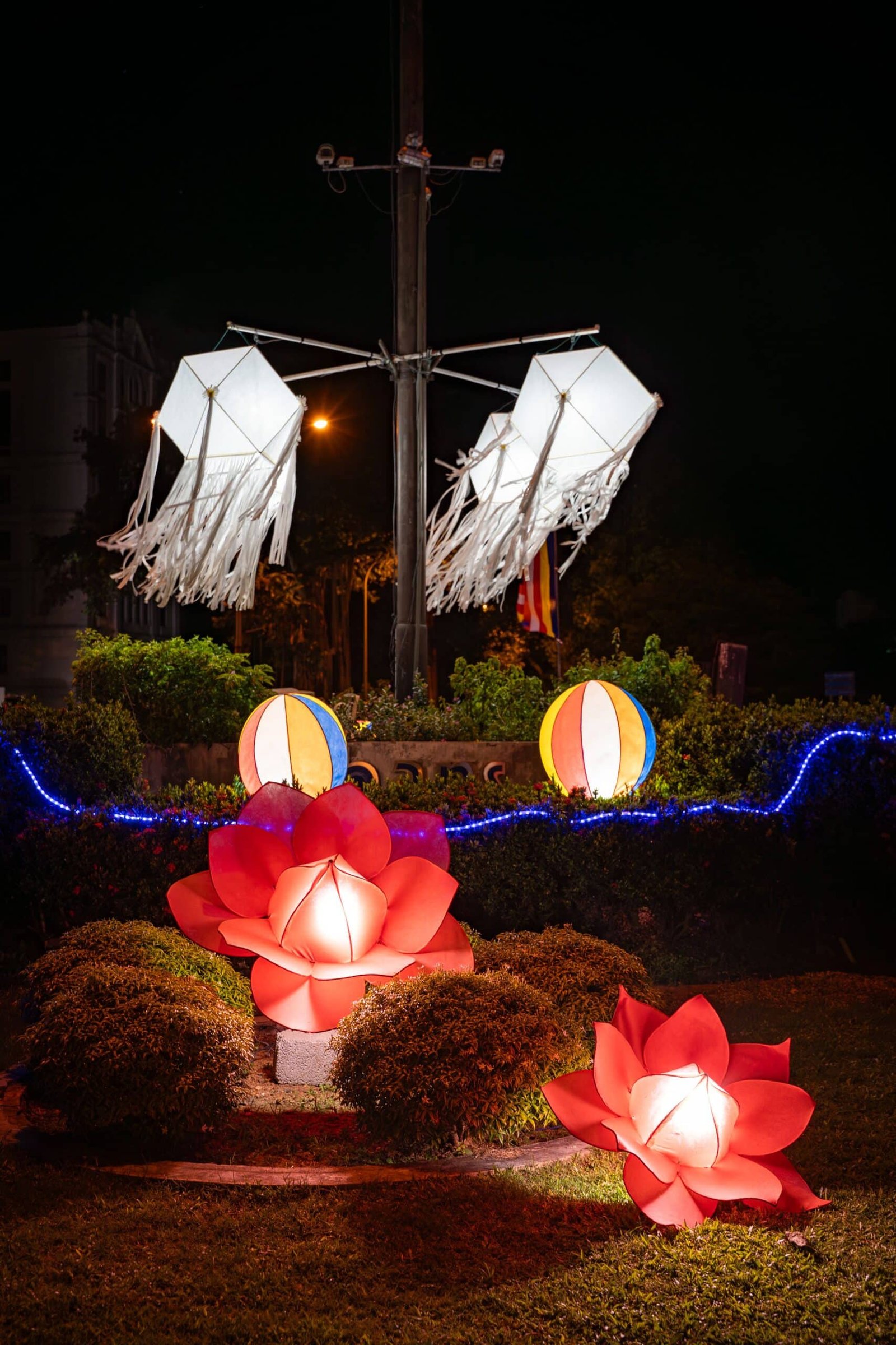 Glowing lotus lights beneath illuminated ship sails in a nighttime garden display.