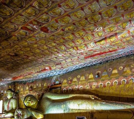 Reclining Buddha statue inside an ancient Buddhist cave temple with ornate painted murals.