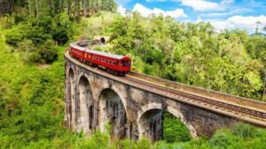Red passenger train crossing a historic stone viaduct amid lush mountain forests.