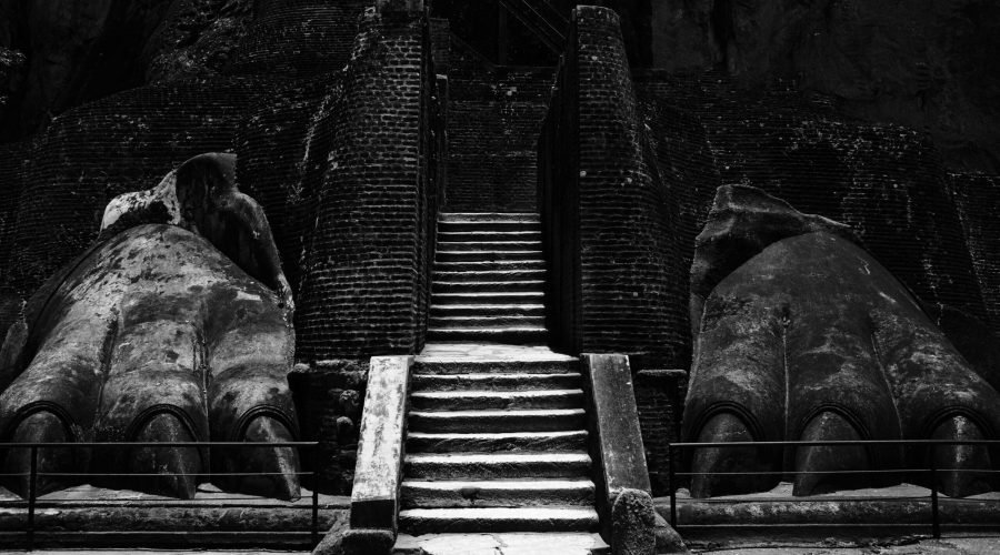 Ancient stone staircase flanked by weathered mythical guardian sculptures in dramatic black-and-white.