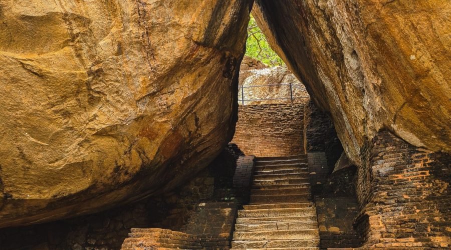 Ancient stone staircase ascends through giant weathered boulders toward sunlit greenery.