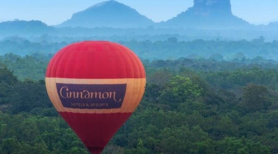 Cinnamon hot-air balloon soaring above a lush tropical forest and misty mountain peaks.