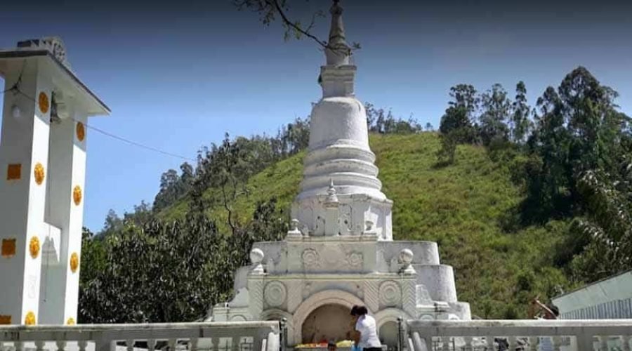 Dhowa Rock Temple stupa against a lush hillside beneath dark storm clouds.