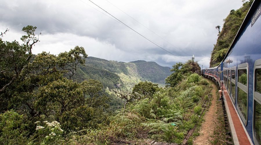 Colorful train winds through lush mountain highlands near Ella, Sri Lanka.