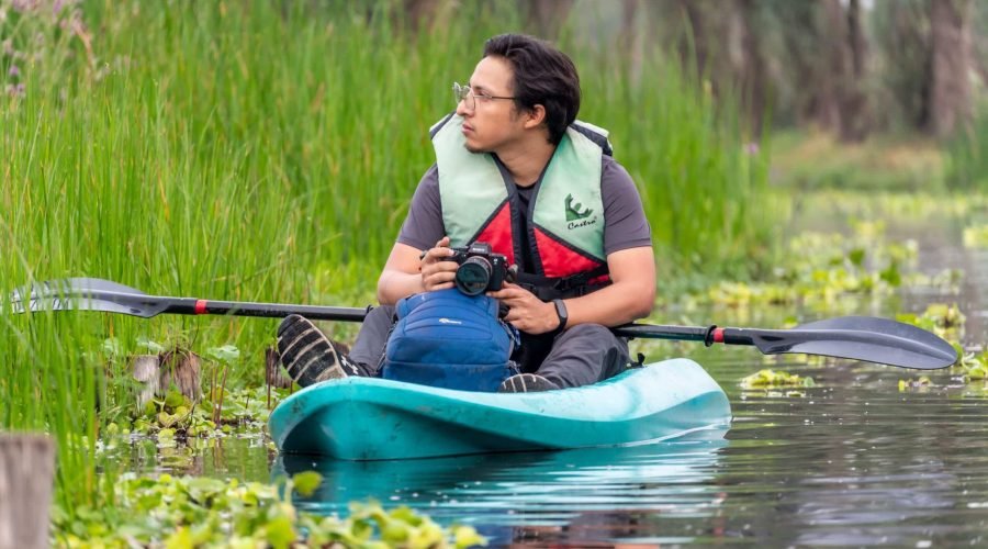 Kayaker in a turquoise kayak paddles through a peaceful green marsh.