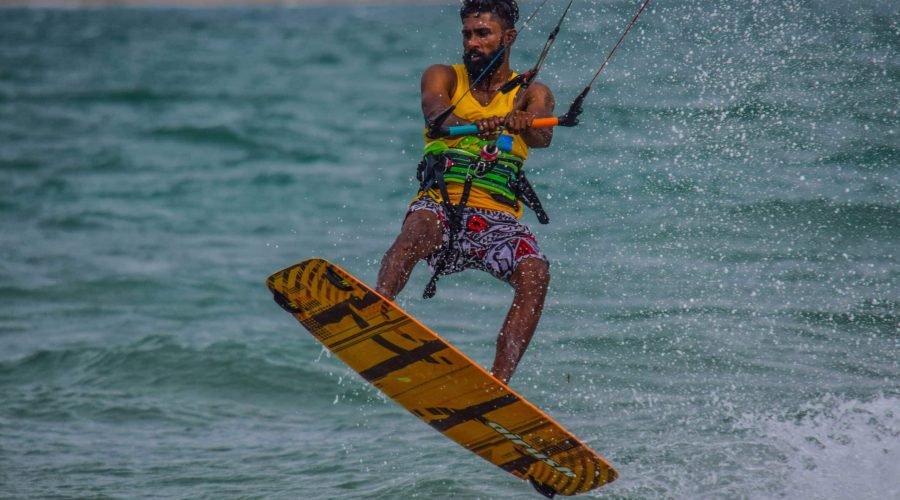 Kiteboarder jumping above choppy turquoise ocean waves on an orange board.
