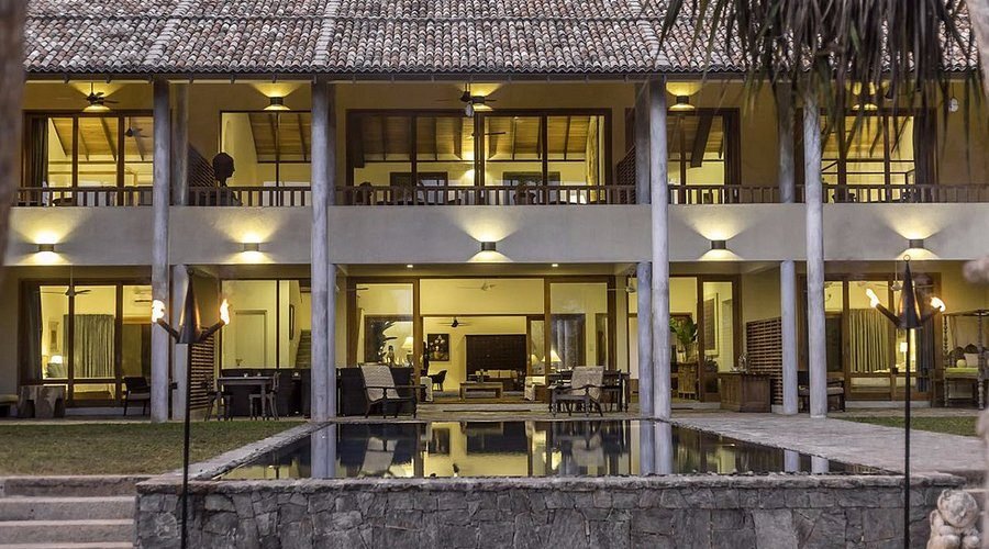 Luxury two-story villa with illuminated glass doors and reflecting pool at dusk.