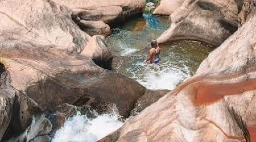 Mountain stream rushes through a granite gorge past hikers and massive weathered boulders.