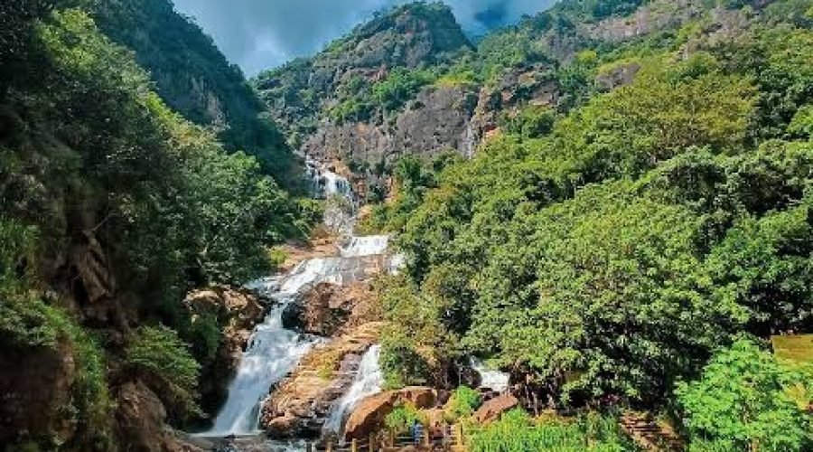 Rocky mountain stream cascades through a lush green valley beneath dramatic clouds.