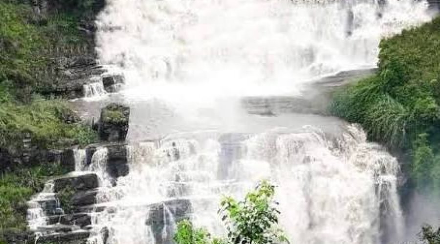 Majestic multi-tier waterfall cascading over dark rocks amid lush green vegetation.