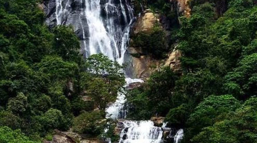 Multi-tiered waterfall cascading through lush rainforest and rugged mountain cliffs.