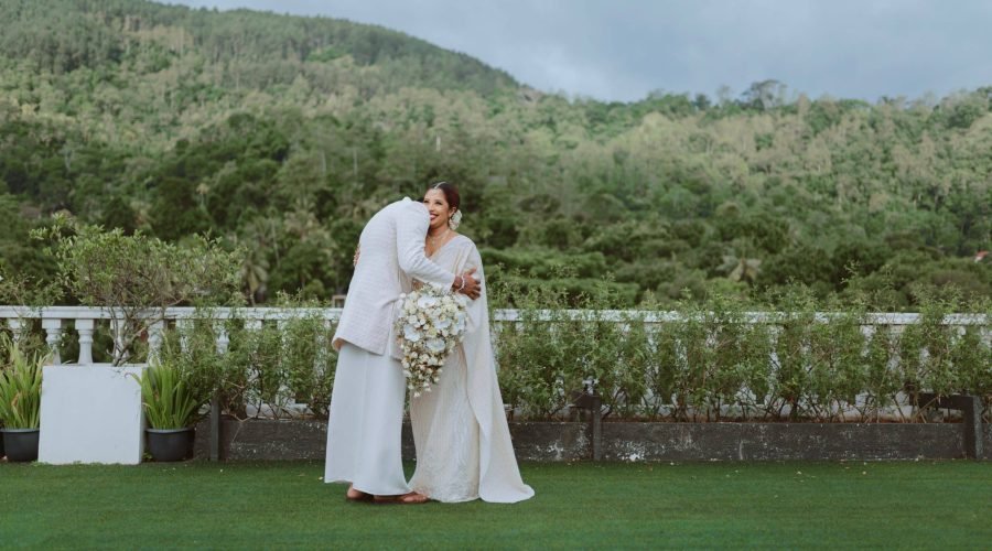 Newlywed couple kissing on a lush lawn with a forested mountain backdrop.