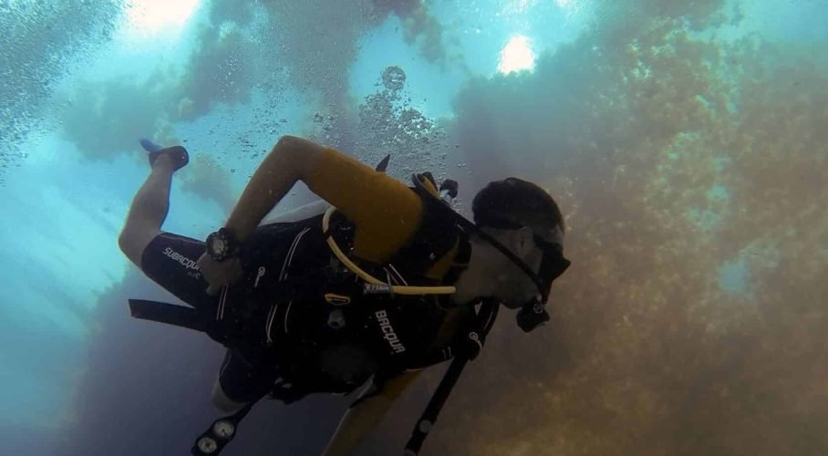 Scuba diver swimming beneath a sunlit ocean surface in deep blue water.