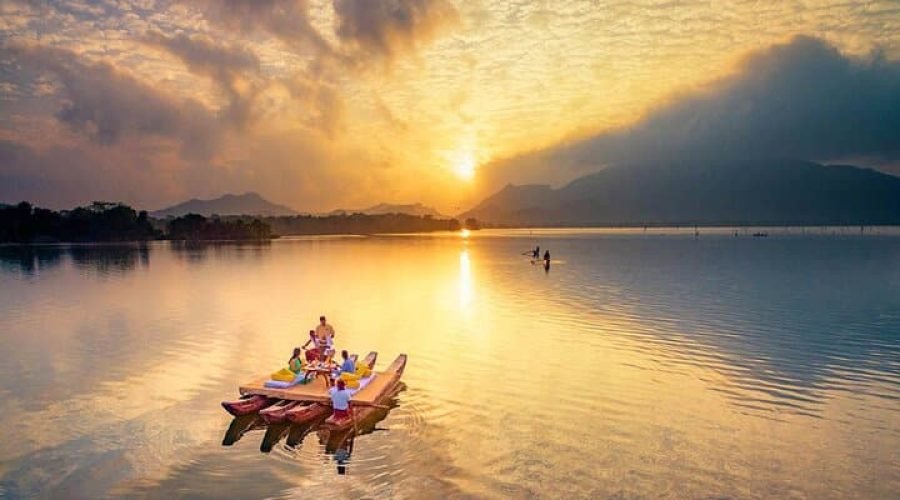 Kayakers paddle across a tranquil mountain lake beneath a dramatic golden sunset.