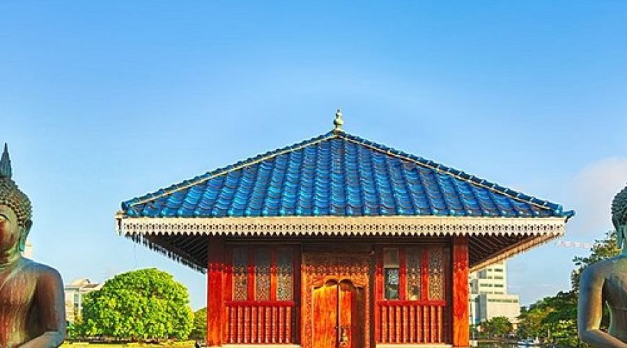 Traditional red pavilion with blue roof framed by seated Buddha statues and reflecting pool.