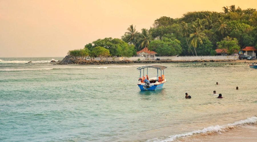 Colorful boat floating near swimmers on a tranquil tropical beach with turquoise water.
