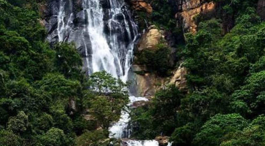 Majestic tropical waterfall cascading down a rugged cliff surrounded by lush green forest.