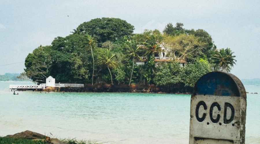 Tropical shoreline overlooking turquoise water, lush island, and weathered CCD concrete marker.