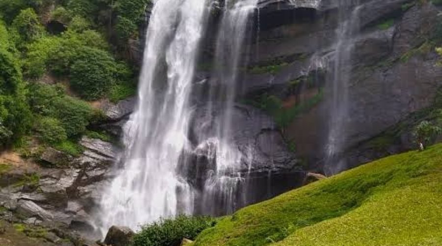 Majestic tropical waterfall cascading down dark cliffs amid lush green forest and hillside.
