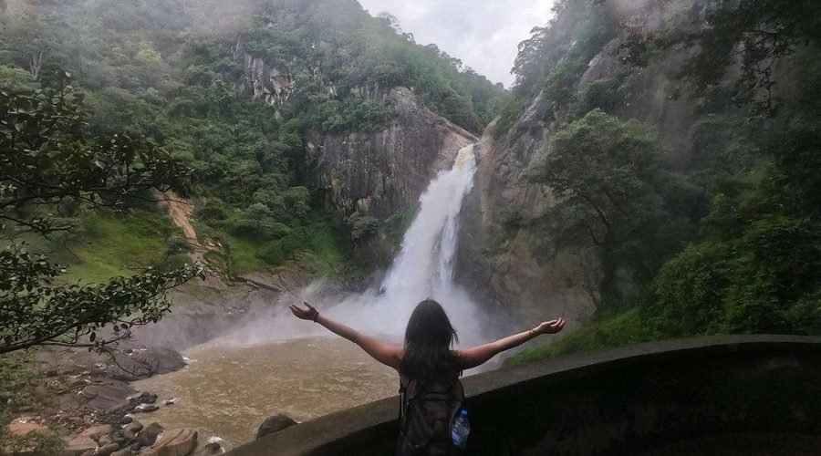 Traveler overlooks a tropical waterfall cascading between lush forested cliffs.