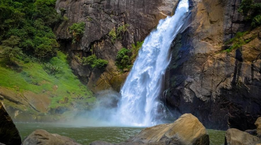 Majestic waterfall cascading between rugged cliffs into a tranquil green pool.