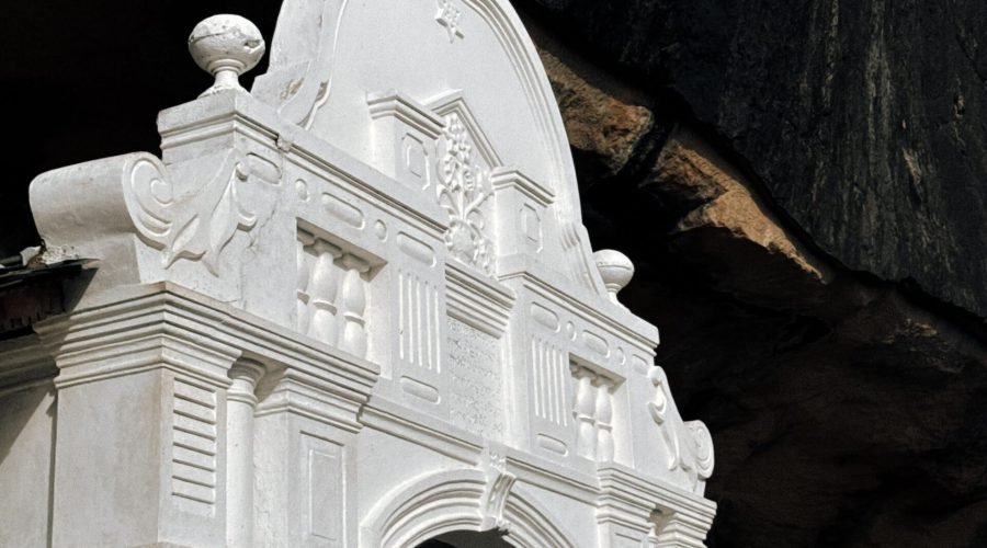 Ornate white temple entrance beneath a massive overhanging cave rock.