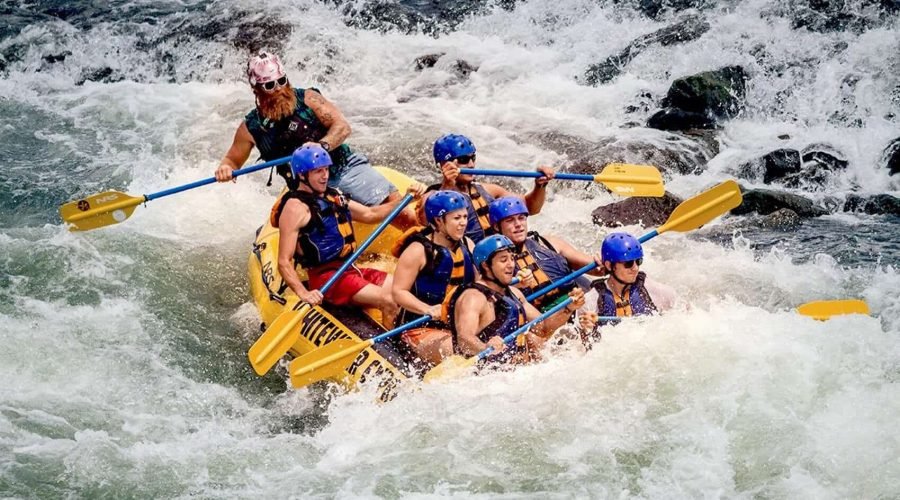 Whitewater rafters paddle a yellow inflatable raft through churning river rapids.
