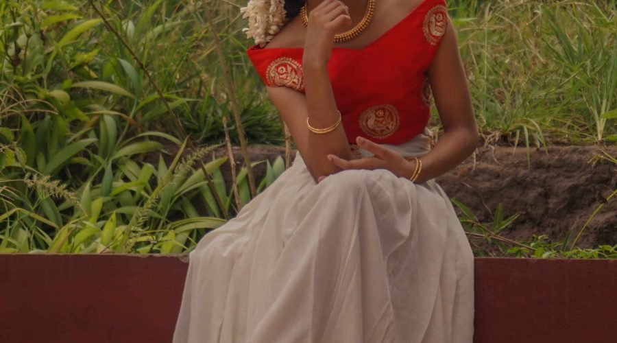 Smiling woman in traditional red blouse and white skirt outdoors.